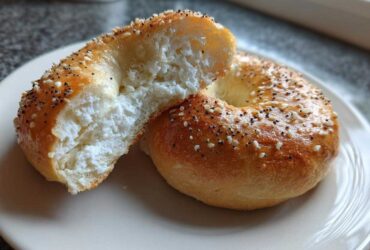 A close-up of a Cottage Cheese Bagels Breakfast, sliced in half to show the fluffy, white cottage cheese interior, topped with seeds.