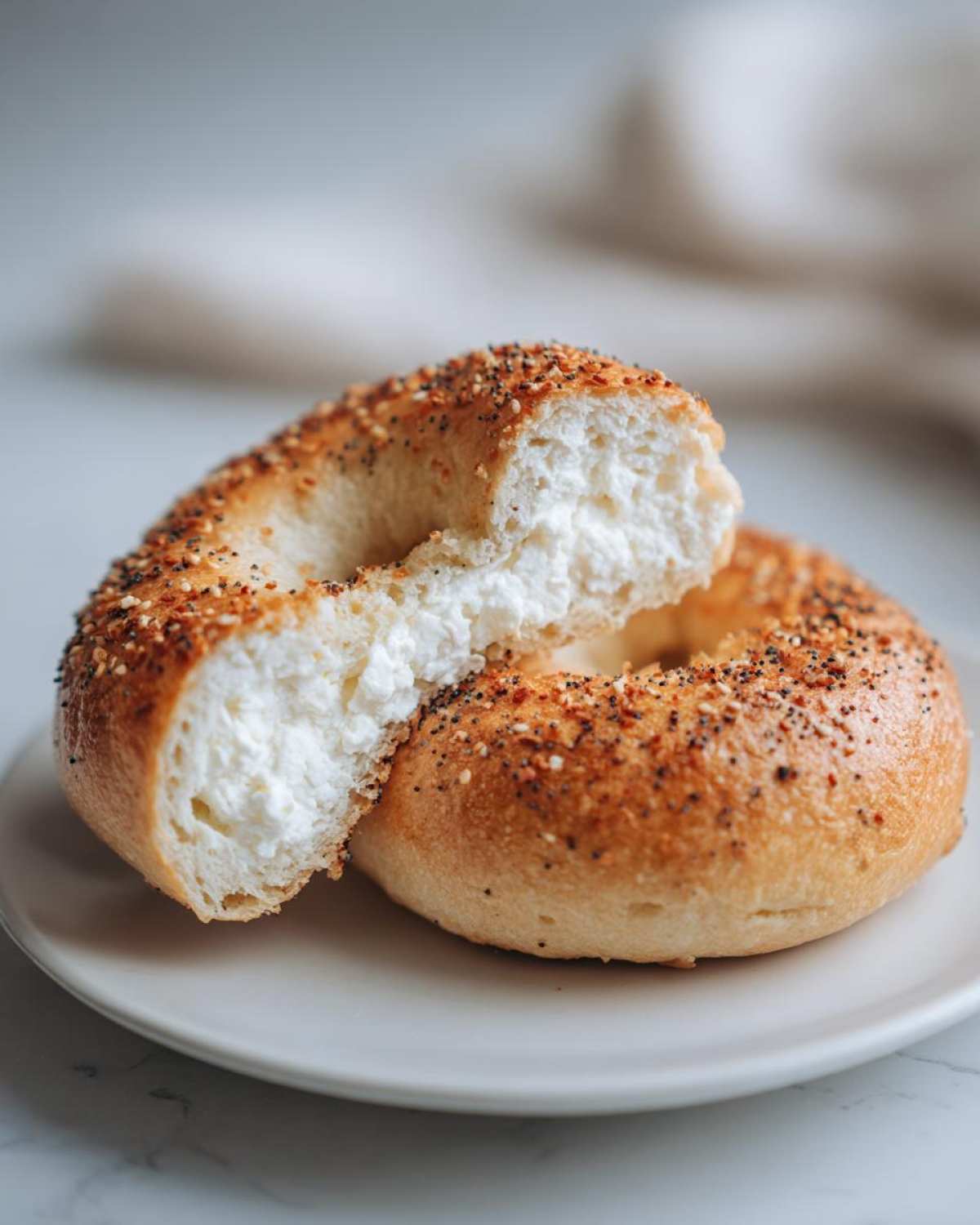 A cottage cheese bagel breakfast, sliced in half to show the fluffy interior and cream cheese filling, topped with everything seasoning.