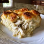 A close-up of a serving of creamy chicken Casserole Crescent Rolls with a golden, cheesy top on a white plate.