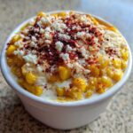 Close-up of a white cup filled with Creamy Mexican Street Corn Esquites Elote, topped with cotija cheese and chili powder.
