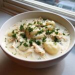 A close-up of a white bowl filled with creamy soup fuss crockpot gnocchi chicken, topped with fresh parsley.