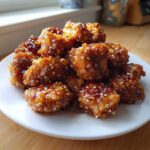 A pile of glistening Crispy Honey Garlic Salmon Bites coated in a thick, sweet glaze and sprinkled with sesame seeds on a white plate.