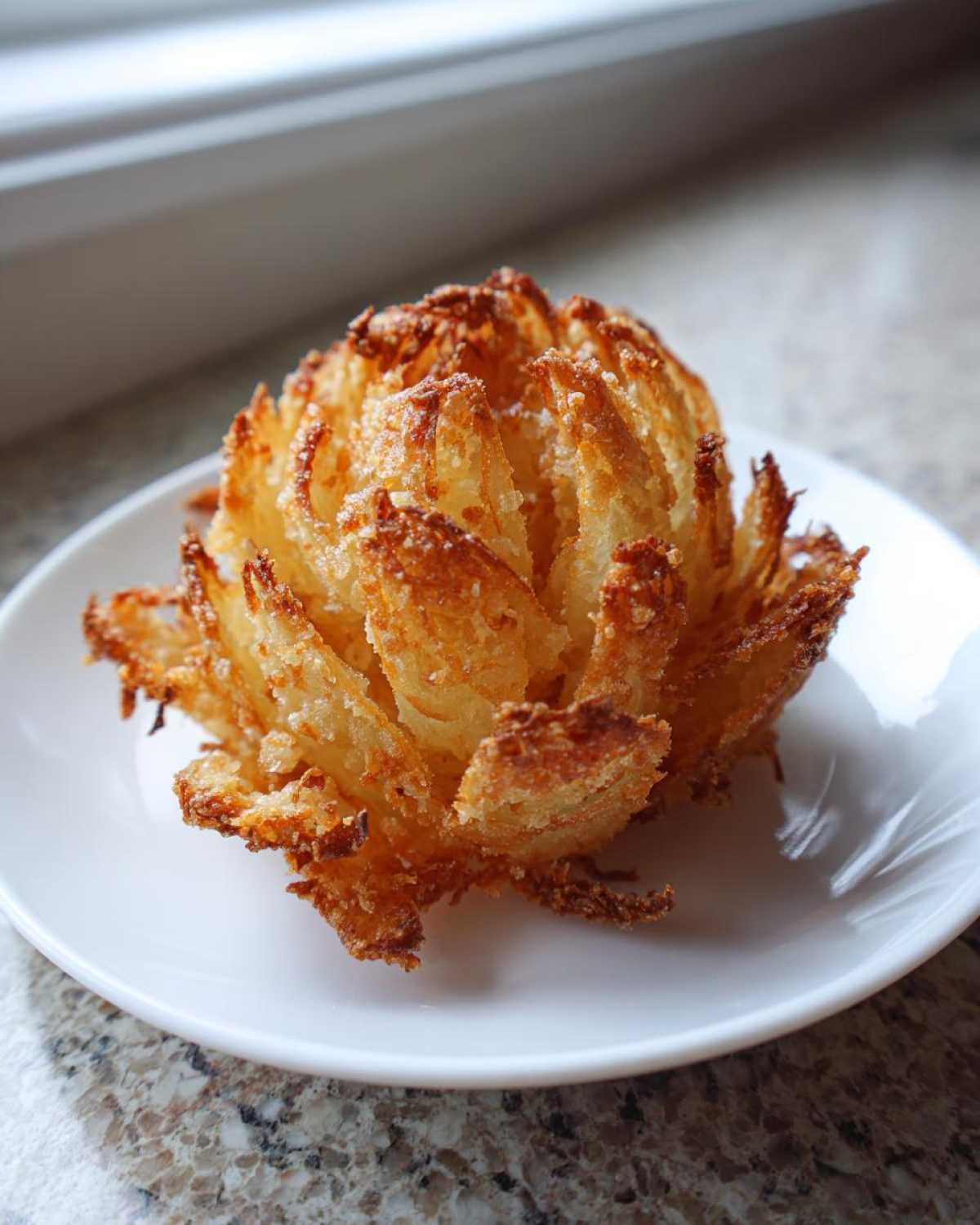 A single, golden-brown, crispy mini blooming onion served on a white plate.
