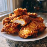 A mound of golden brown Crispy Waffle Batter Fried Chicken on a white plate, one piece broken open showing juicy white meat.