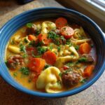 A close-up of rich Crockpot Sausage Tortellini Soup with carrots, meatballs, and fresh parsley garnish in a blue bowl.