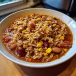 A close-up of a white bowl filled with hearty Crockpot Taco Rice Soup, featuring ground meat, rice, kidney beans, and corn in a savory broth.