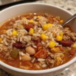 Close-up of a white bowl filled with Crockpot Taco Rice Soup, featuring rice, ground meat, corn, and beans in a rich broth.