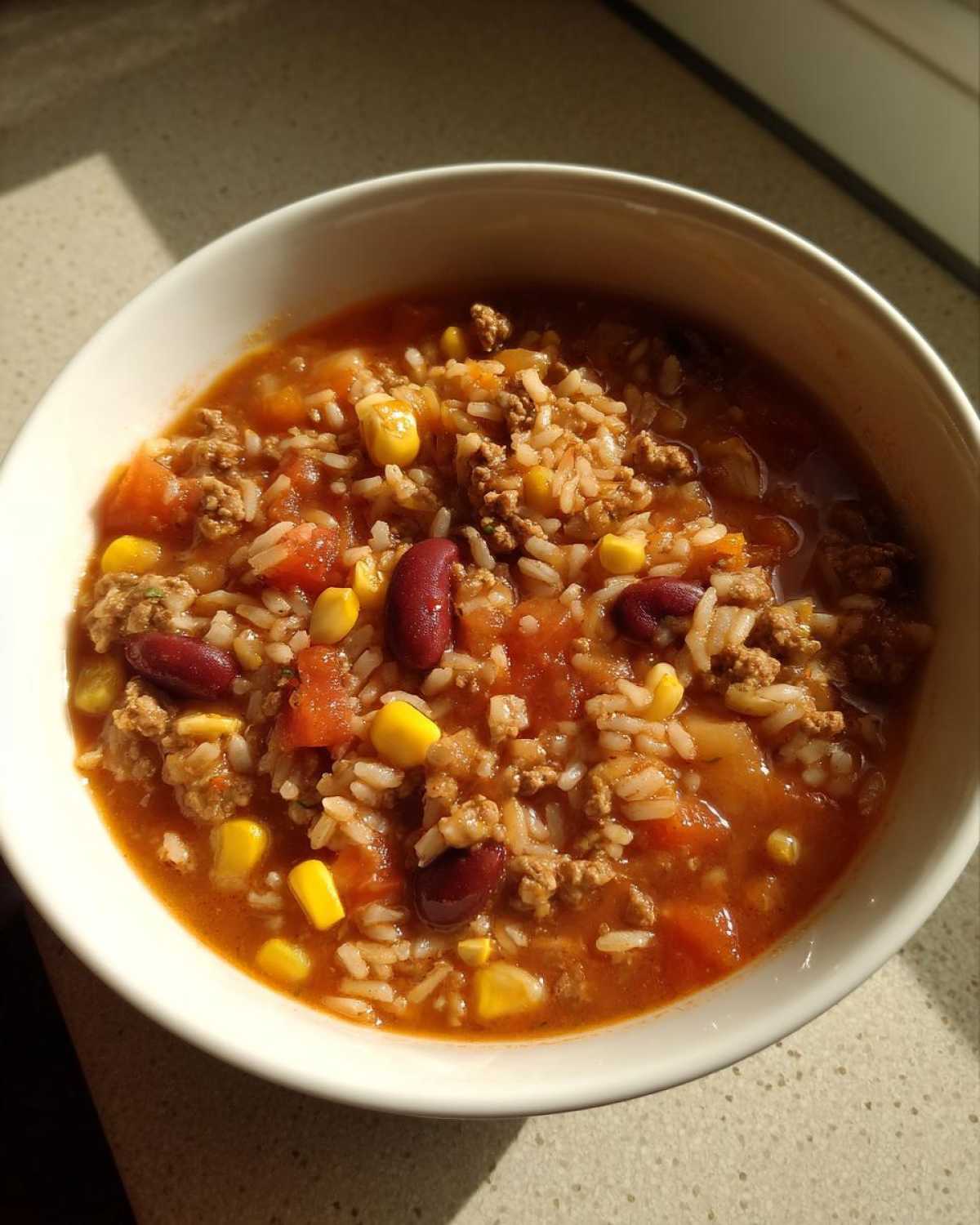 Close-up of a white bowl filled with Crockpot Taco Rice Soup featuring ground meat, rice, kidney beans, and corn in a tomato broth.