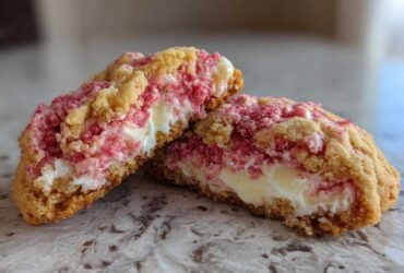 Close-up of Delicious Strawberry Cheesecake Cookies cut in half, showing a creamy white center and pink strawberry crumble topping.