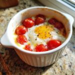 A close-up of an Easy 5-Minute Microwave Egg Caprese Cups recipe cooked in a white ramekin with cherry tomatoes.