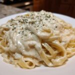 Close-up of fettuccine pasta coated in creamy Easy Cottage Cheese Alfredo Sauce and sprinkled with herbs.