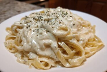 Close-up of fettuccine pasta coated in creamy Easy Cottage Cheese Alfredo Sauce and sprinkled with herbs.