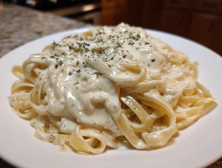 Close-up of fettuccine pasta coated in creamy Easy Cottage Cheese Alfredo Sauce and sprinkled with herbs.