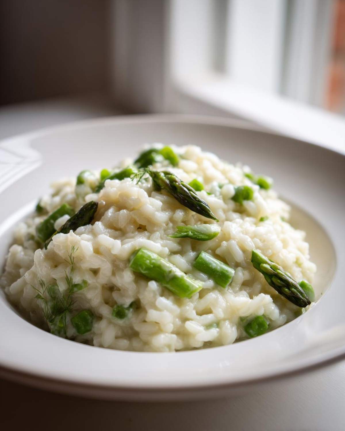 A close-up of a bowl of Easy Creamy Asparagus Risotto topped with bright green asparagus tips and dill.