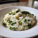 A close-up of a serving of Easy Creamy Asparagus Risotto with bright green asparagus pieces in a white bowl.