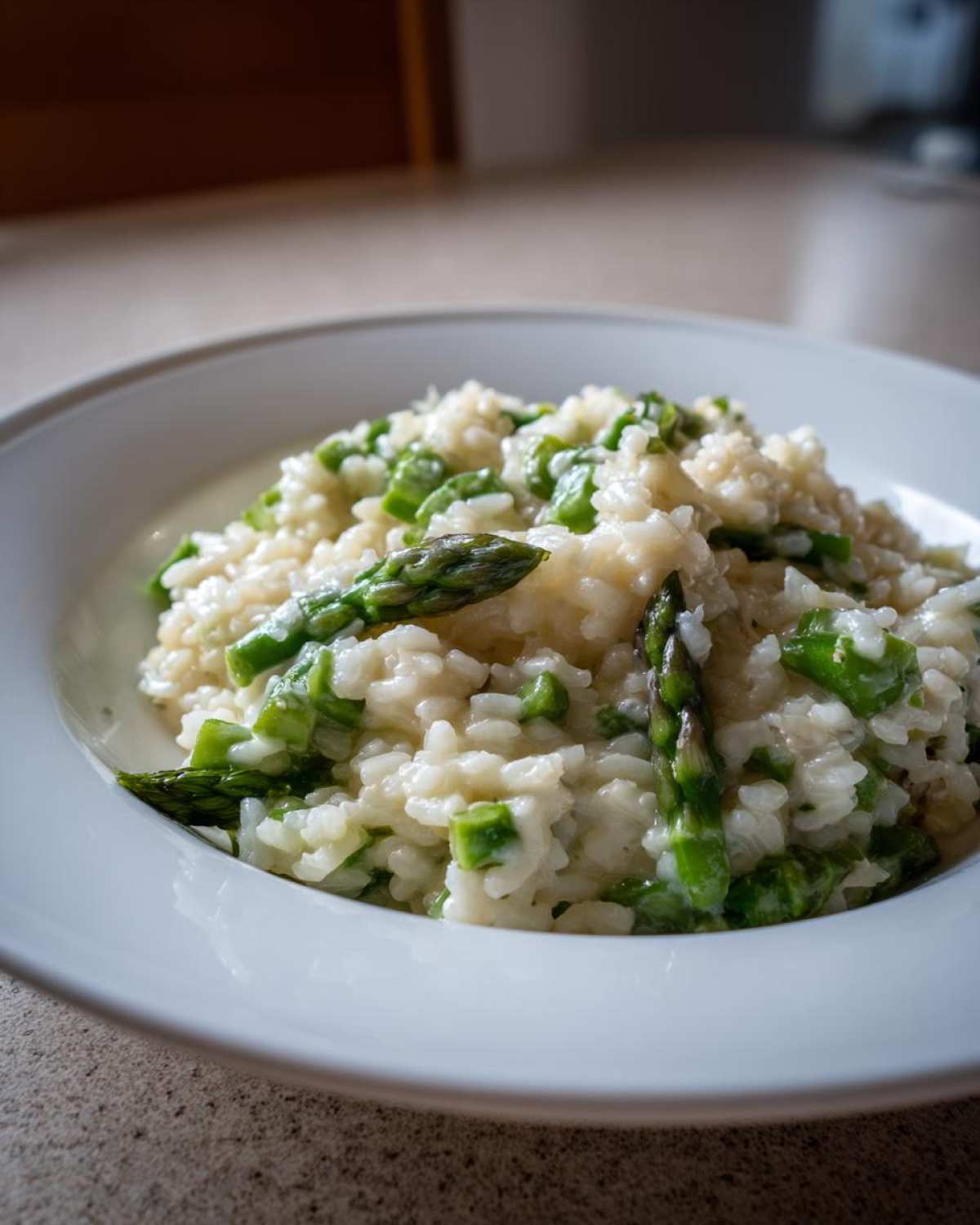 A close-up of a white bowl filled with Easy Creamy Asparagus Risotto, featuring creamy rice and bright green asparagus pieces.