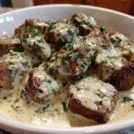 Close-up of seared steak bites smothered in creamy garlic sauce and sprinkled with fresh parsley.