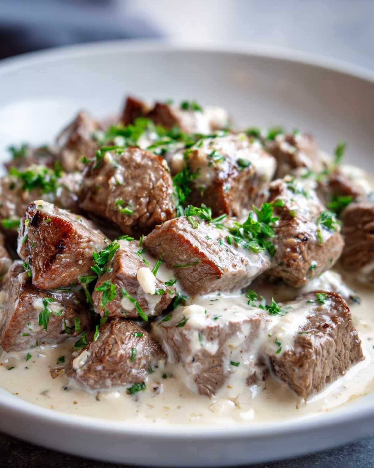 Close-up of juicy steak bites coated in Easy One-Pan Creamy Garlic Steak Bites sauce and topped with fresh parsley.