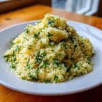 A mound of fluffy, yellow Easy One-Pot Creamy Lemon Herb Couscous topped generously with chopped fresh parsley.