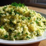 A close-up of fluffy Easy One-Pot Creamy Lemon Herb Couscous garnished with fresh green herbs and yellow lemon zest.