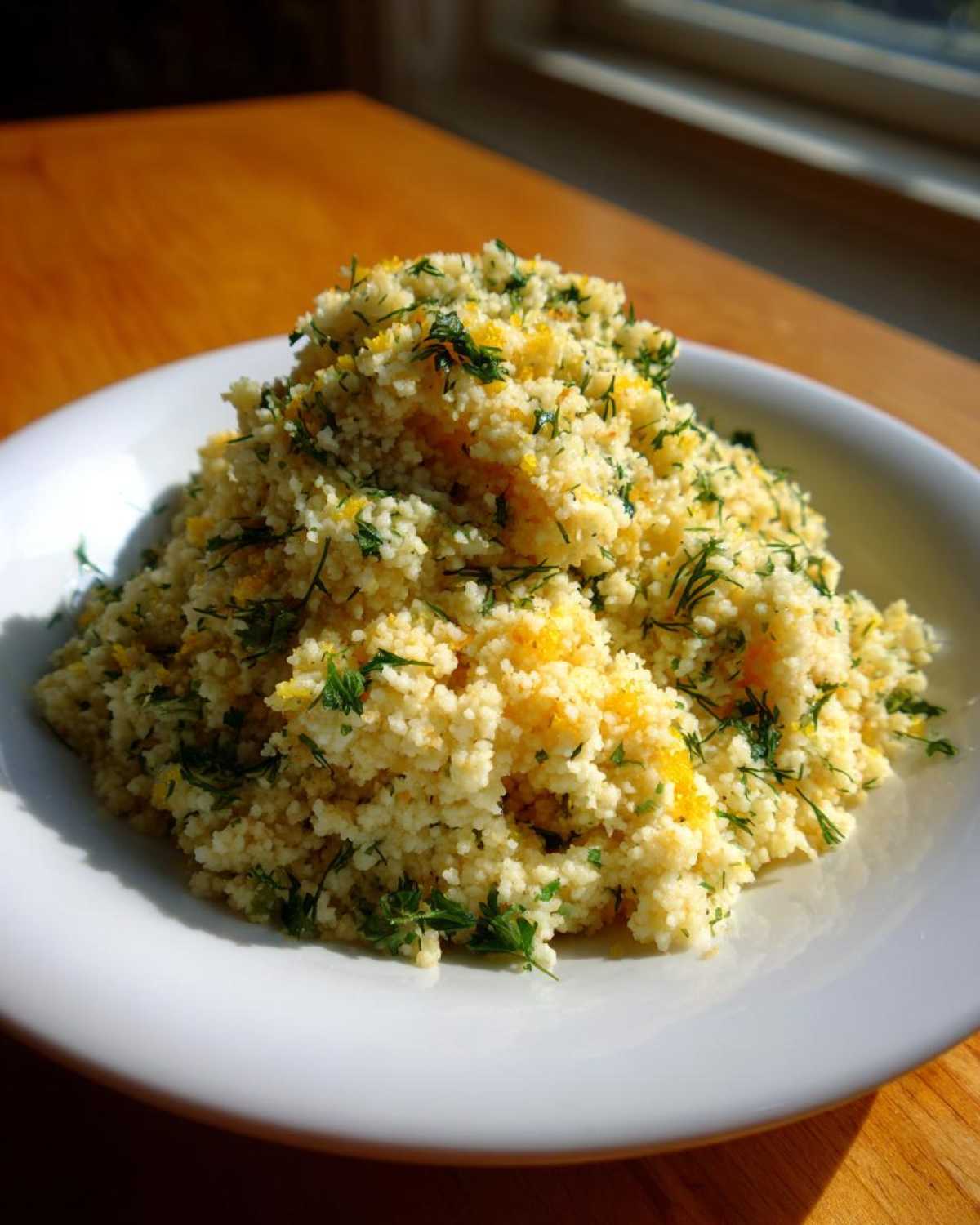 A mound of Easy One-Pot Creamy Lemon Herb Couscous garnished with fresh green herbs and bright yellow lemon zest.