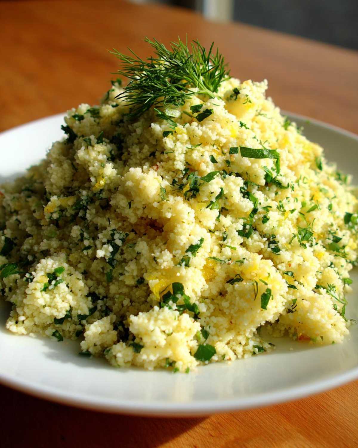 A mound of fluffy Easy One-Pot Creamy Lemon Herb Couscous garnished with fresh dill on a white plate.