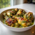 Close-up of browned chicken drumsticks covered in bright green salsa verde sauce in a white bowl.