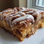 A close-up of a square serving of Easy Sheet Pan Cinnamon Roll Pancake Bake topped with white icing.