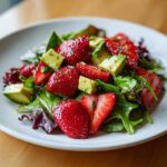 A vibrant close-up of Easy Strawberry Avocado Salad featuring sliced strawberries, diced avocado, and mixed greens tossed in a light dressing.
