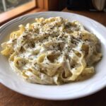 A bowl of fettuccine pasta generously coated in creamy Easy Cottage Cheese Alfredo Sauce and topped with pepper.