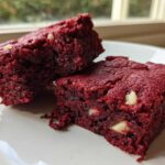 Two rich, fudgy red velvet brownies studded with white chocolate chips resting on a white plate.