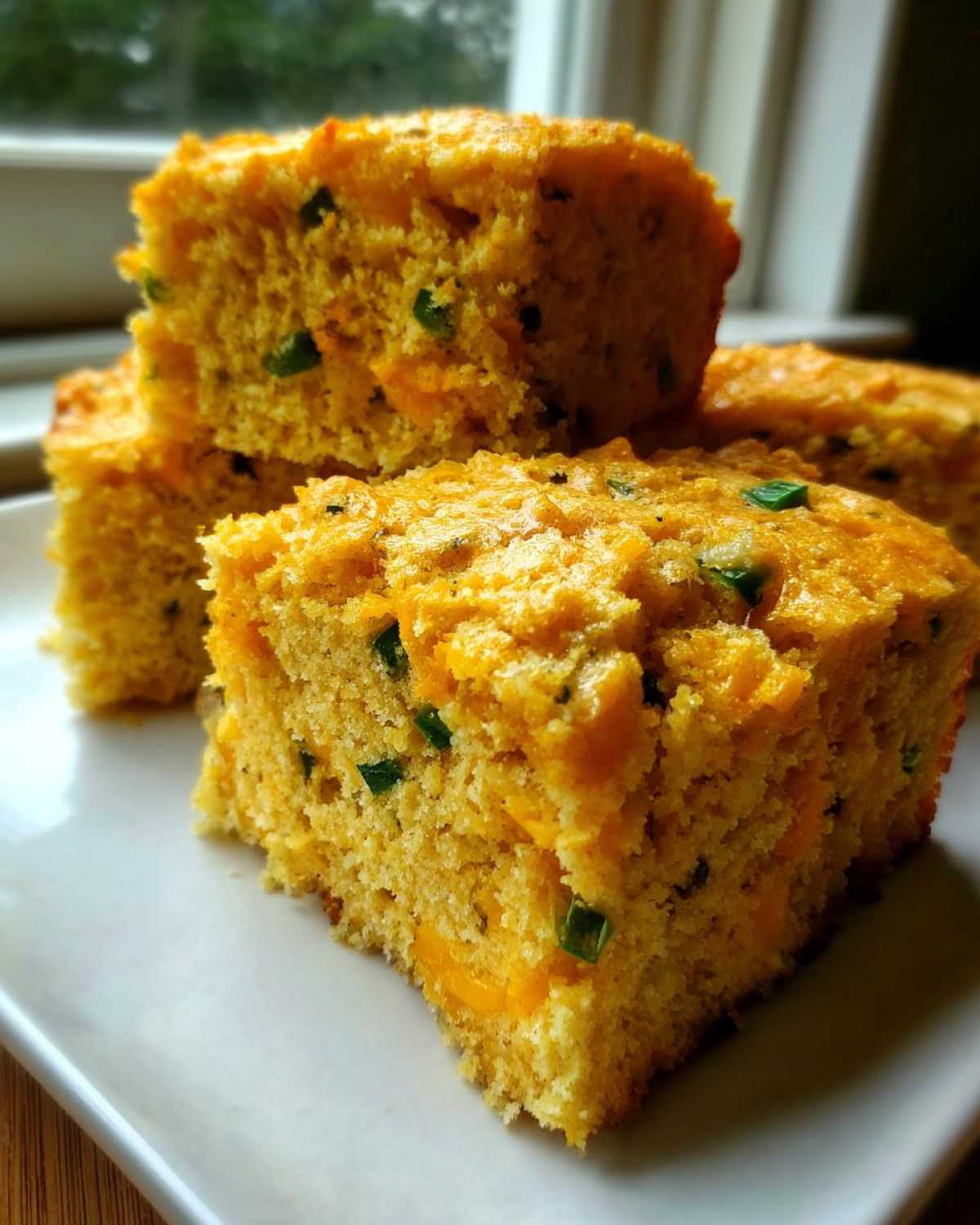 Close-up of stacked squares of moist Gluten-Free Cheddar Jalapeno Cornbread with visible cheese and green jalapeno pieces.