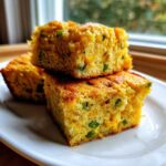 Three moist squares of Gluten-Free Cheddar Jalapeno Cornbread stacked on a white plate, showing visible cheddar cheese and green jalapeno pieces.
