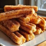 A stack of freshly made Gluten-Free Cinnamon Sugar Waffle Sticks generously coated in cinnamon sugar, sitting on a white plate.