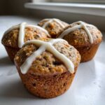 Four freshly baked Gluten-Free Hot Cross Bun Muffins topped with a white icing cross, displayed closely.