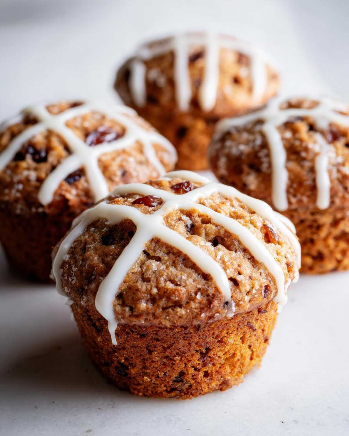 Several freshly baked Gluten-Free Hot Cross Bun Muffins topped with white icing crosses and coarse sugar