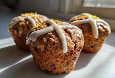 Three freshly baked Gluten-Free Hot Cross Bun Muffins topped with white icing crosses and orange zest.