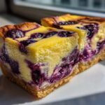 Two rich squares of Gluten-Free Lemon Blueberry Cheesecake Squares with a thick crust, sitting on a white plate.
