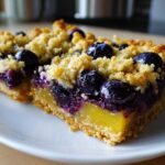 Two slices of Gluten-Free Lemon Blueberry Layer Bars showing a thick crust, bright lemon filling, and blueberry crumble topping.