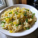 A white bowl filled with bright Gluten-Free Lemon Pepper Fried Rice, topped with yellow lemon zest and green scallions.