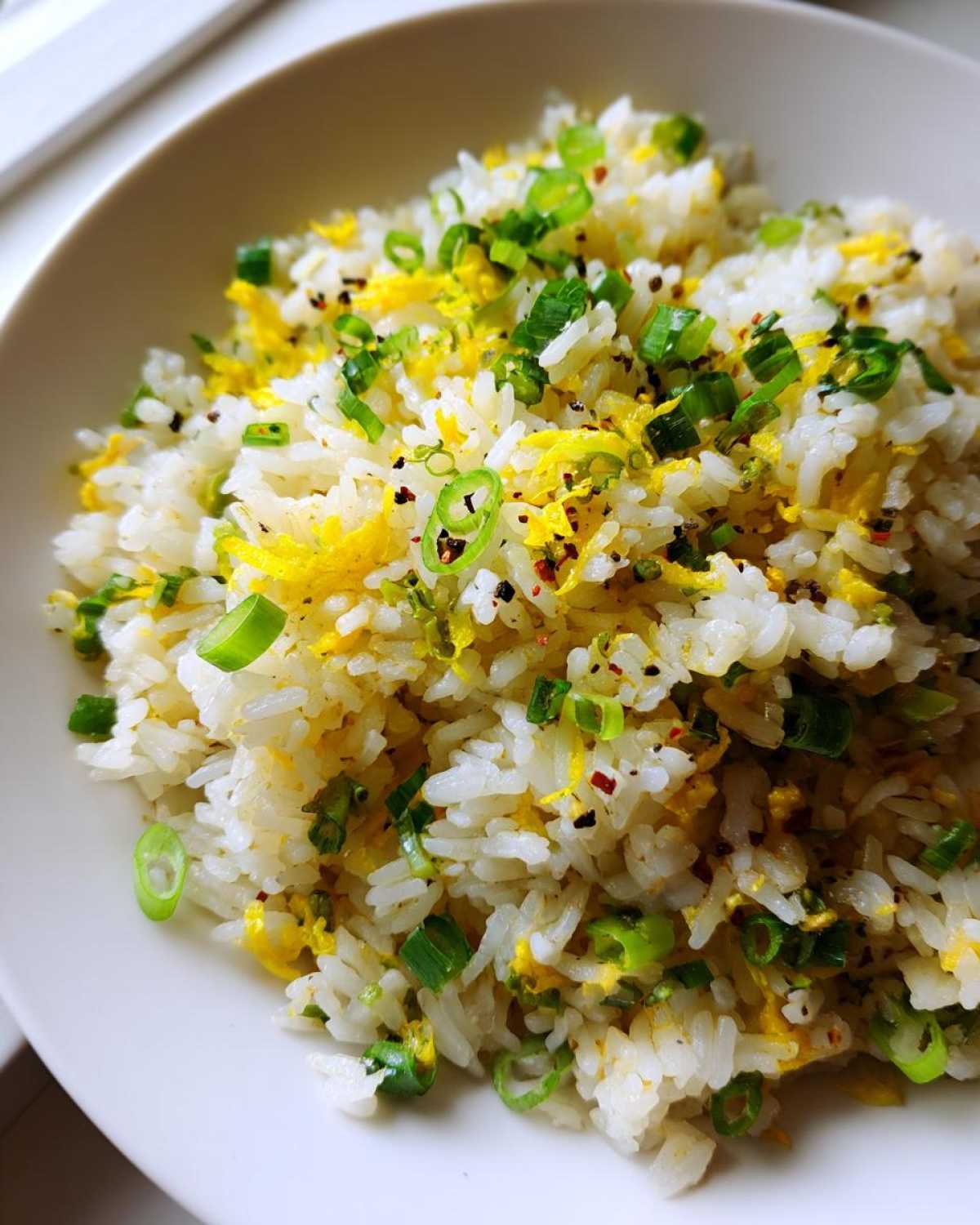 A close-up view of fluffy white rice tossed with scrambled egg, bright green scallions, and yellow lemon zest in Gluten-Free Lemon Pepper Fried Rice.