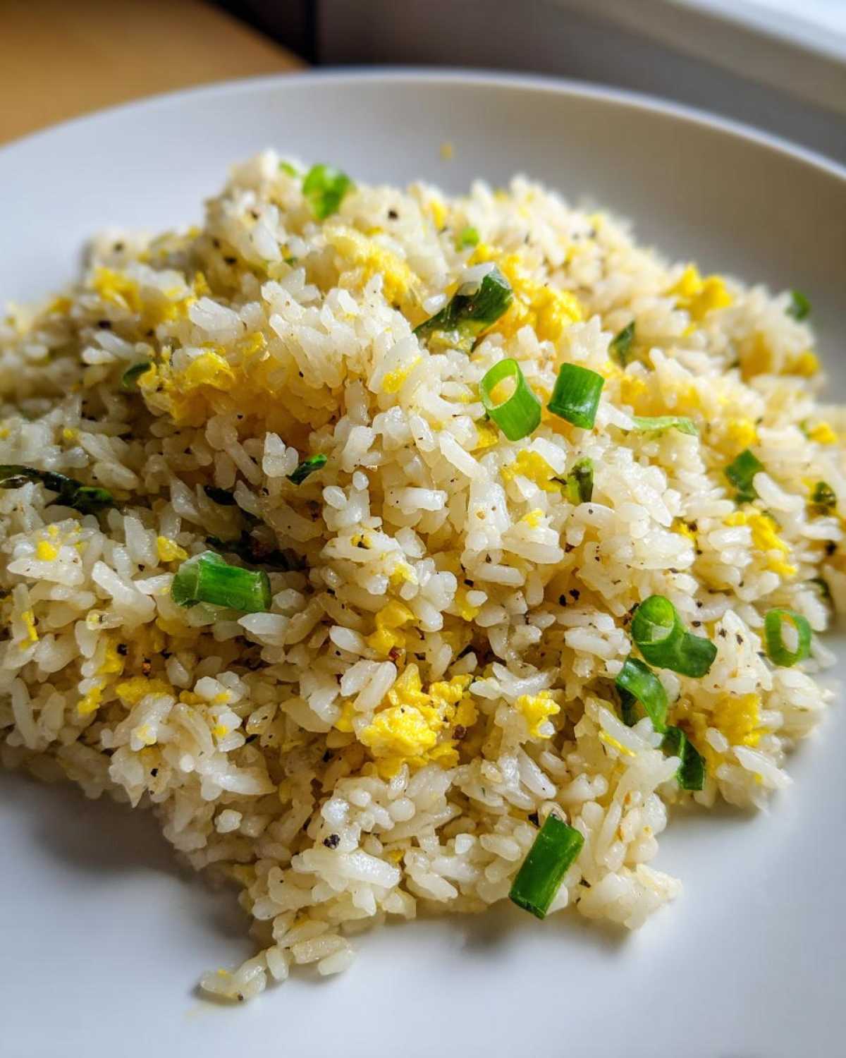 A close-up of fluffy Gluten-Free Lemon Pepper Fried Rice mixed with scrambled egg pieces and topped with bright green scallions.