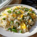 A close-up of a serving of Gluten-Free Lemon Pepper Fried Rice mixed with scrambled egg and topped with chopped green onions.