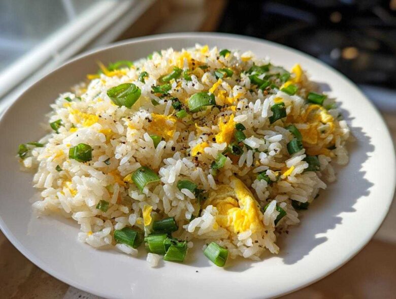 A close-up of a serving of Gluten-Free Lemon Pepper Fried Rice mixed with scrambled egg and topped with chopped green onions.