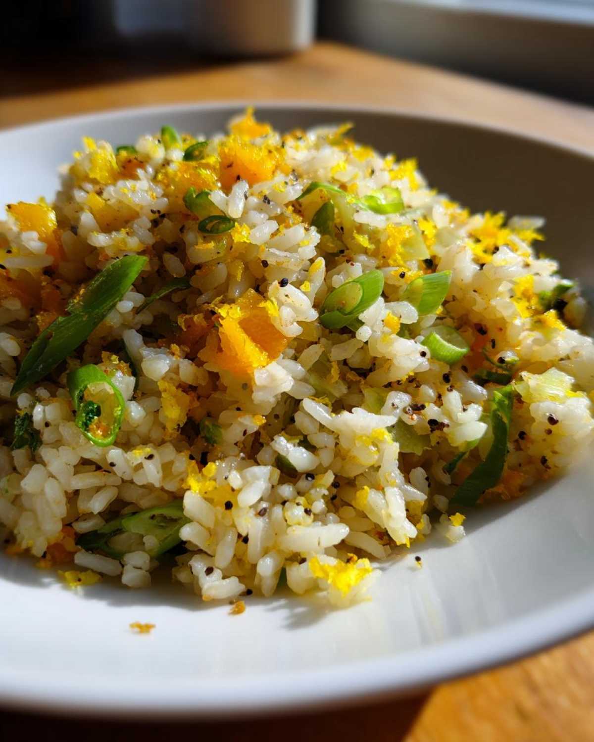 A close-up of Gluten-Free Lemon Pepper Fried Rice garnished with bright yellow lemon zest and green scallions.