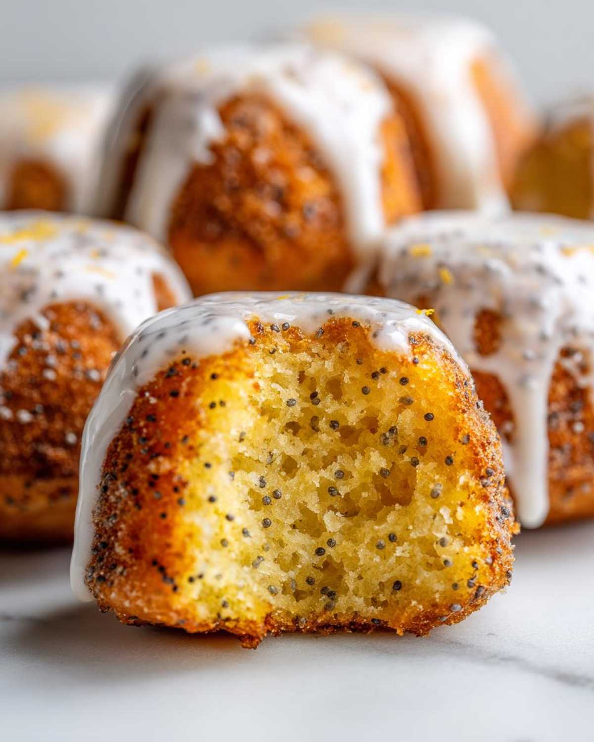 Close-up of a Gluten-Free Lemon Poppy Seed Donut Hole with a bite taken out, showing the moist interior and lemon glaze.