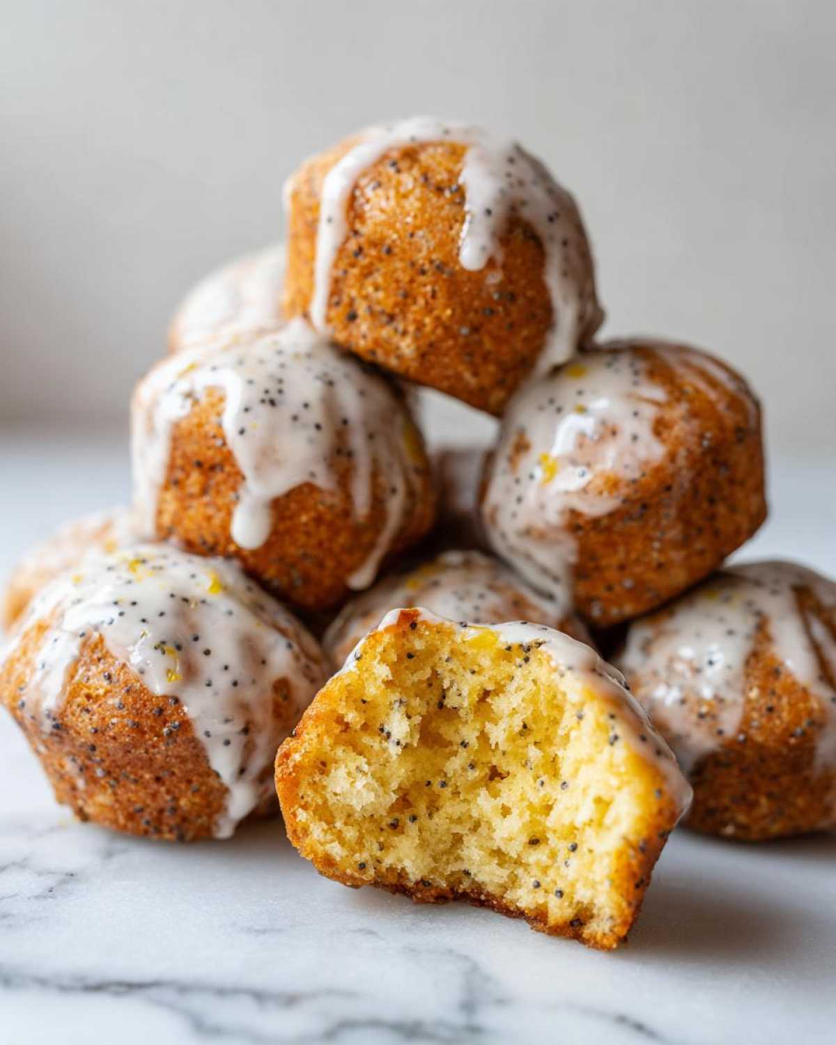 A stack of moist Gluten-Free Lemon Poppy Seed Donut Holes drizzled with lemon glaze, one bitten open.