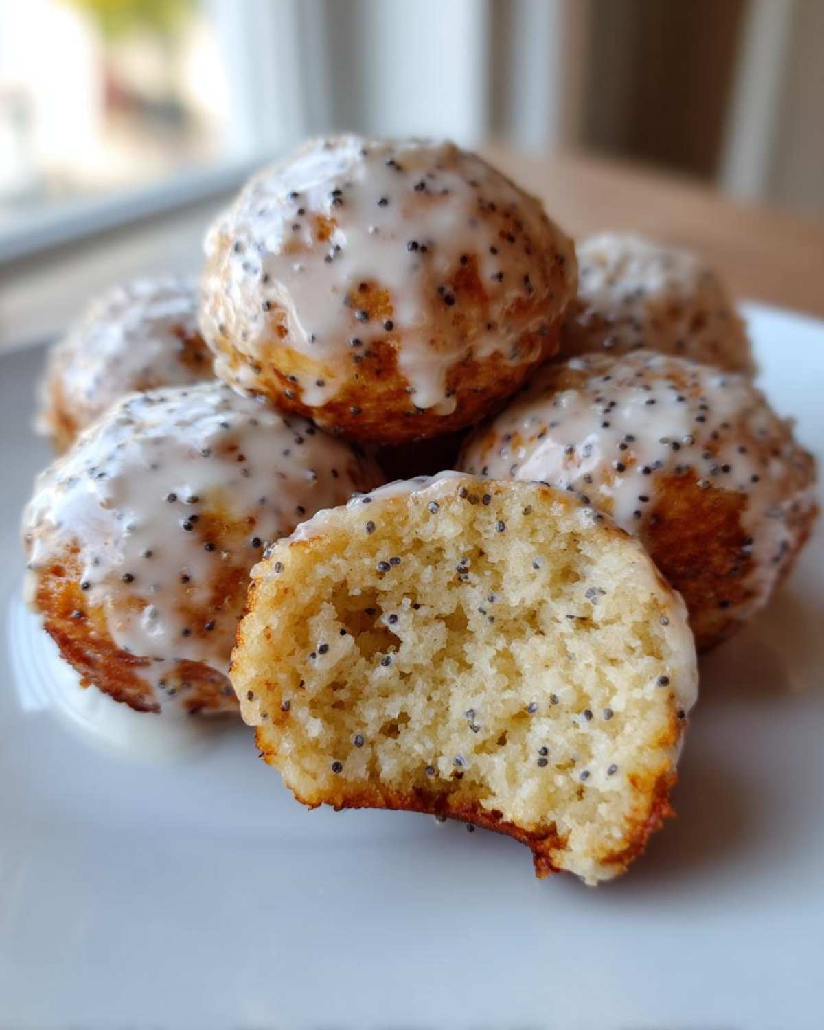 Close-up of stacked Gluten-Free Lemon Poppy Seed Donut Holes with lemon glaze and visible poppy seeds.