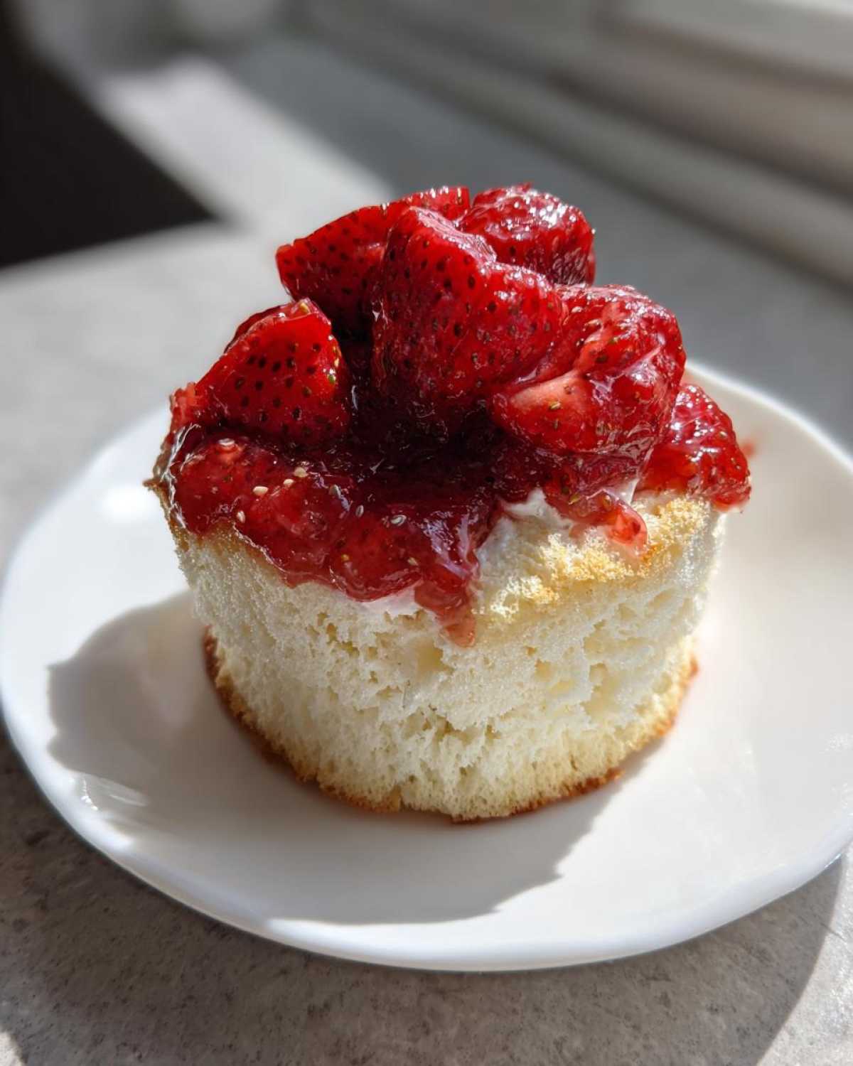 A single Gluten-Free Lemon Strawberry Angel Food Cup topped with macerated strawberries on a white plate.