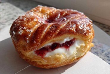 Close-up of a golden brown Gluten-Free Strawberry Cream Cheese Danish filled with white cream cheese and strawberry jam.